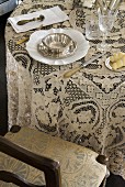 Lace tablecloth and vintage place setting next to upholstered chair