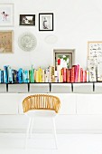 White wicker chair in front of books arranged by colour on wall-mounted shelf