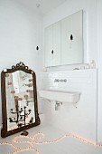 Light rope on floor next to antique mirror leant against wall in bathroom