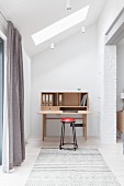 Simple desk and stool in niche below sloping ceiling