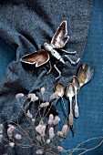Metal insect figurine and vintage silver spoons on dark fabric