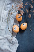 Easter eggs decorated with animal stickers and dried twig on blue fabric