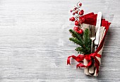 Table fork and knife set with napkin, christmas fir branch, red berries and ribbon on gray wooden background