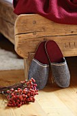 Grey felt slippers leant against rustic wooden bed