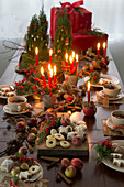 Weihnachtlicher Tisch mit Kerzen, Plätzchen, Ilex, Äpfeln und Apfeltee