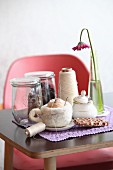 DIY Gefilzte Tasse mit Milchhäubchen, Schokolade, Zuckerdose, Gerbera, Garn und Glasbehälter auf Tisch