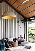 Woman and child on sofa in high living room with trapezoidal sheet cladding next to patio door in industrial style