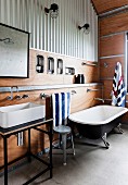 Vintage bathtub and vanity with countertop basin in the bathroom with trapezoidal sheet cladding and with wooden cladding