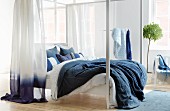 Four-poster bed with blue and white linen and curtains