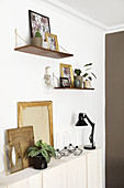 Wall-mounted shelves above sideboard and pictures with backs turned to room