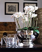 White orchids planted in silver bowl next to glass jug