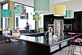 Black modern kitchen area in centre of room below colourful lampshades