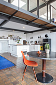 Dining table and designer chair in front of open-plan kitchen below mezzanine