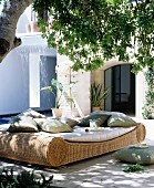Comfortable wicker lounger with cushions in dappled shade below a tree