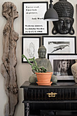 Feminine wooden sculpture next to Buddha statue on console table and black-framed photos and quotes on wall