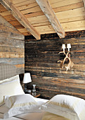 Wandleuchte aus Geweih an rustikaler Holzwand im Schlafzimmer