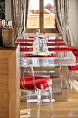 Moderne transparente Essgruppe mit roten Kissen und Tischsets