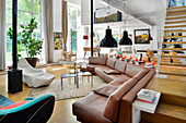 Brown leather corner sofa and designer armchairs in open-plan interior