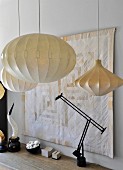 Black table lamp and various pendant lamps in front of quilted wall hanging