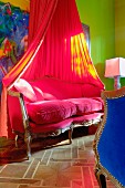 Baroque sofa with pink upholstery, heart-shaped cushions and canopy in front of colourful painting