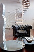 Round mirrored table and leather armchair in front of spiral staircase