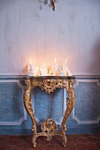 Arrangement of white candles of various shapes on antique gilt console table