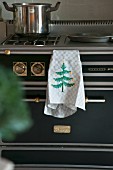Tea towel with embroidered Christmas tree hung on black gas cooker