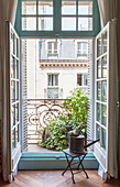 Hocker mit Gießkanne vor offener Balkontür mit Blick aufs Nachbarhaus