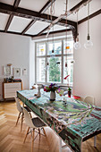 Colourful tablecloth on long table, classic chairs and pendant lamps with light bulbs in dining room