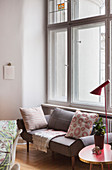 Sofa mit Kissen, Beistelltisch und Stehleuchte vor Fenster in Altbauwohnung