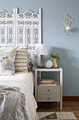 Bett und Betthaupt mit ornamentalem Muster neben Nachtkästchen