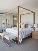 Four-poster bed against patterned wallpaper and antique chest of drawers in country-house-style bedroom