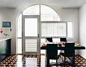 Black chairs and set table on geometric floor tiles in dining area in front of glazed arch with glass door