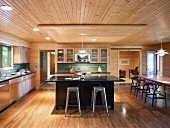 Offene Küche mit schwarzer Küchentheke und Barhockern in hellem renoviertem Holzhaus
