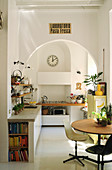Round table, classic chairs, kitchen counter with concrete worksurface and mobile gas cooker in kitchen with arched doorway