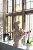 Bust and orchids on sill of old lattice window with stone frame