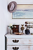 Jewelery on a vintage wooden chest of drawers, picture and hat above