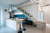 Open-plan, industrial-style kitchen below concrete staircase and extractor hood duct