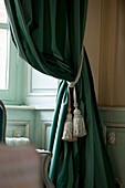 Classic tassels on dark green curtains against panelled wall