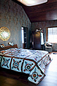 Quilt on bed in bedroom with dark ornate wallpaper
