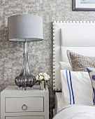 Elegant bedside lamp with glass base next to bed with white headboard