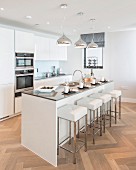Elegante, weiße Einbauküche mit Kücheninsel und Designer-Barhockern