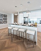 Island counter and designer bar stools in elegant white fitted kitchen