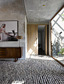 Table lamp on retro sideboard below photo on wall in foyer with concrete walls