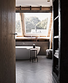 Blick ins Dachgeschoss-Badezimmer mit frei stehender Badewannen unter dem Fenster und Betonboden