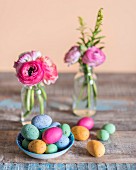 Colourful speckled eggs in bowl in front of posies of ranunculus