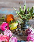 Small Buddha figurine, incense burner and ranunculus flowers on wooden surface