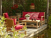 Outdoor furniture with red cushions on wooden terrace next to garden pond