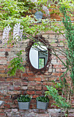 Ovaler Spiegel mit verschnörkeltem Rahmen an Backsteinwand im Garten