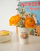 Orange ranunculus and white flowers in retro beaker with printed picture and motto